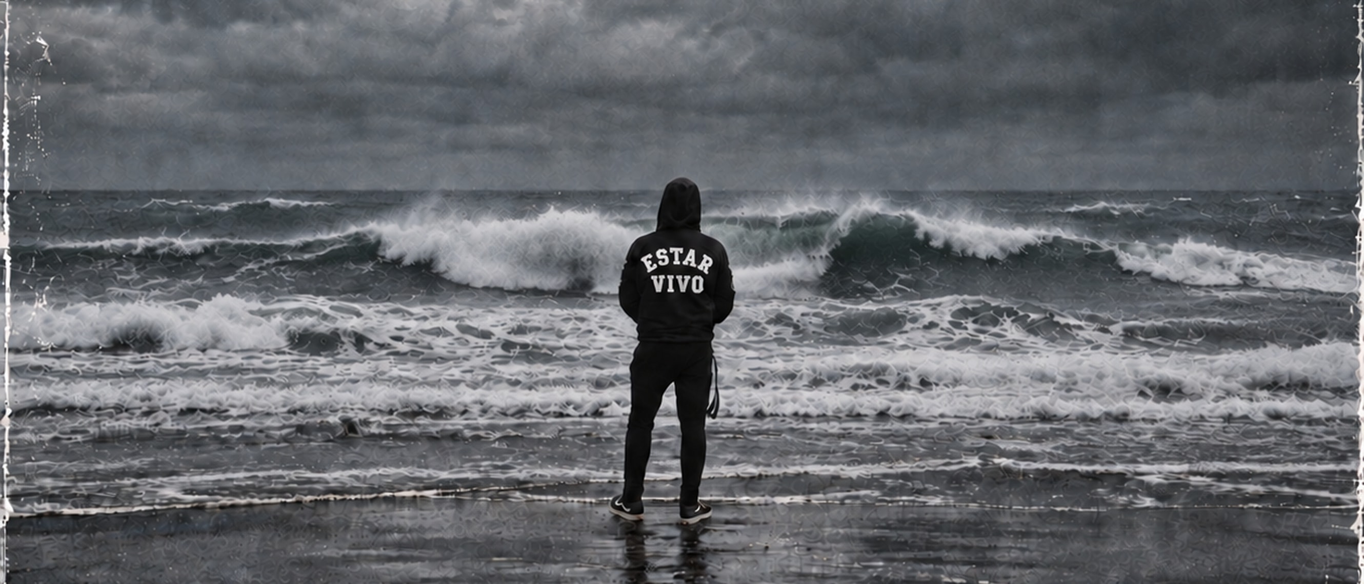 MARTO de espaldas frente a las olas, con «Estar vivo» escrito en la capucha.