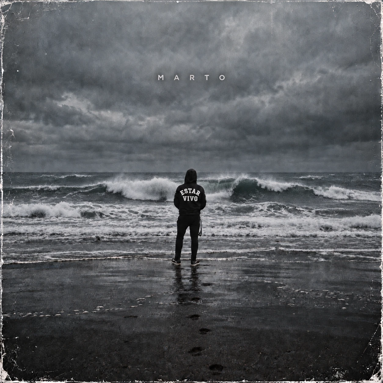 Portada de «Estar vivo» de MARTO: una persona de espaldas con capucha negra frente a un mar de invierno bajo un cielo de tormenta.
